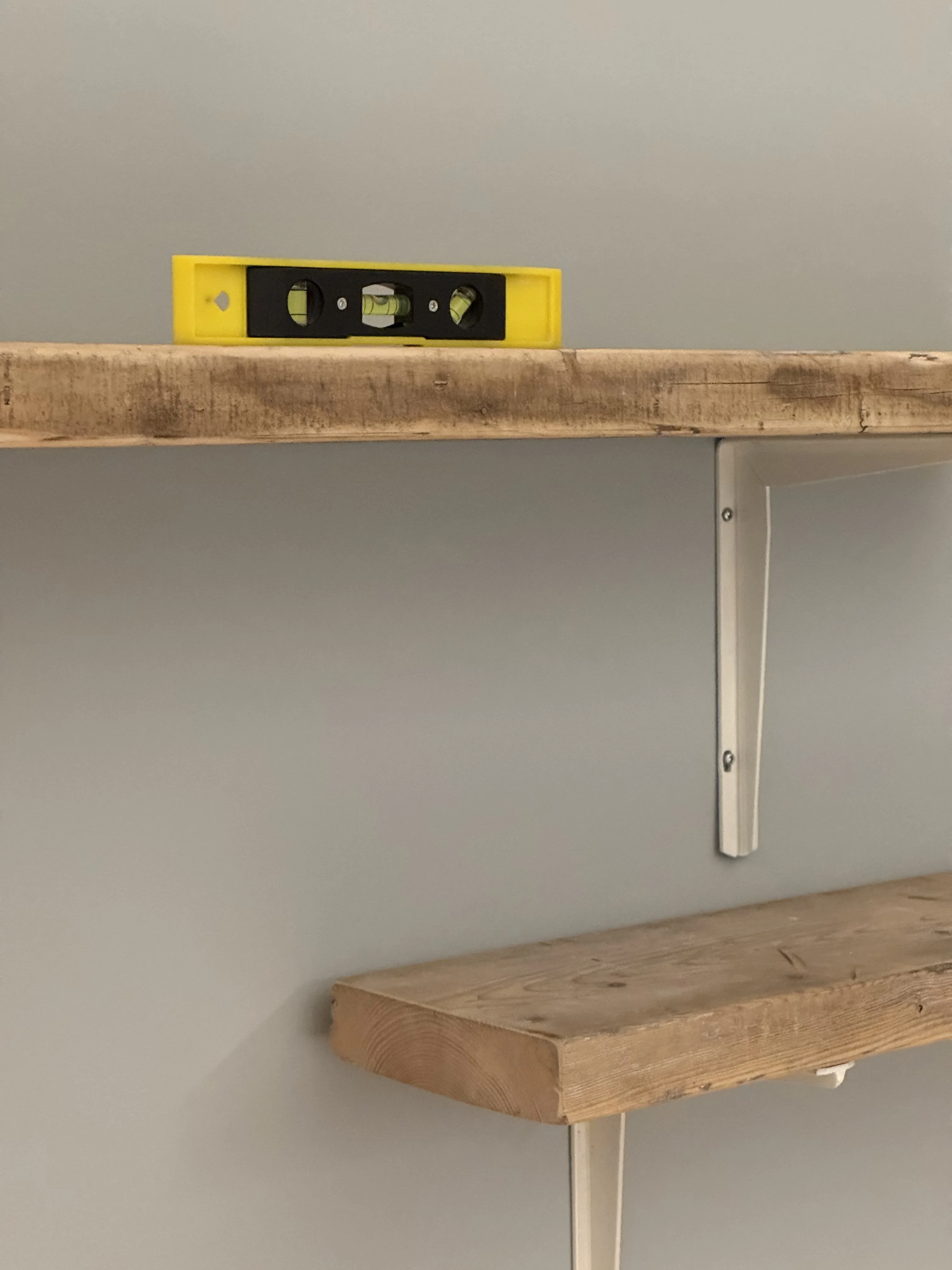 Level check and bracket detail on two installed wood shelves